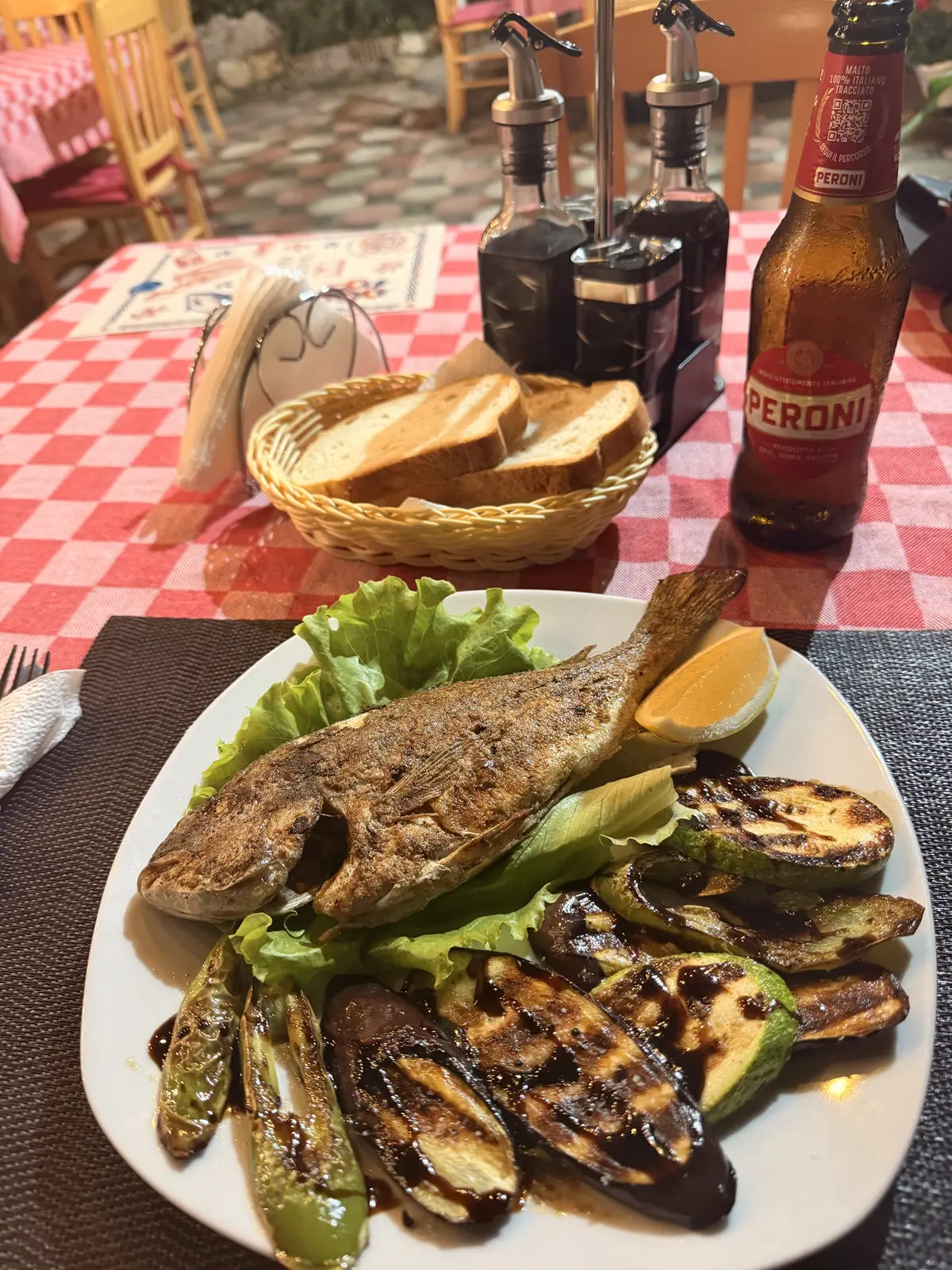 A plate of grilled whole fish with grilled vegetables and a beer at a restaurant in Vlore, Albania.