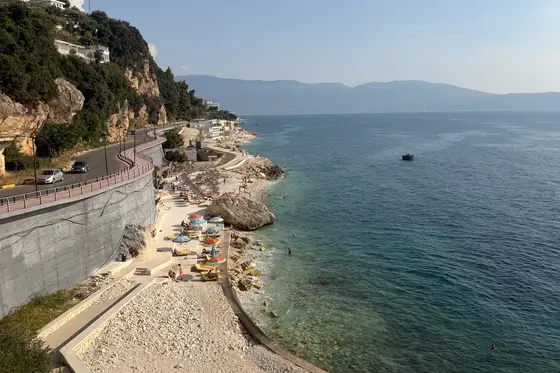 The Albanian Riviera coast road above a small pebble beach with umbrellas and turquoise water near Vlore.