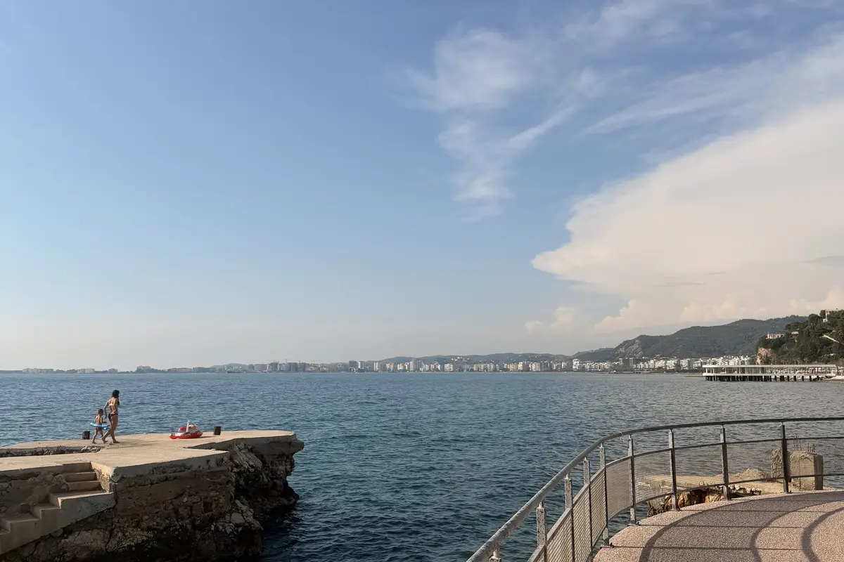The seafront walkway in Vlore, Albania, a mother and child walking along a railed path above the calm bay.