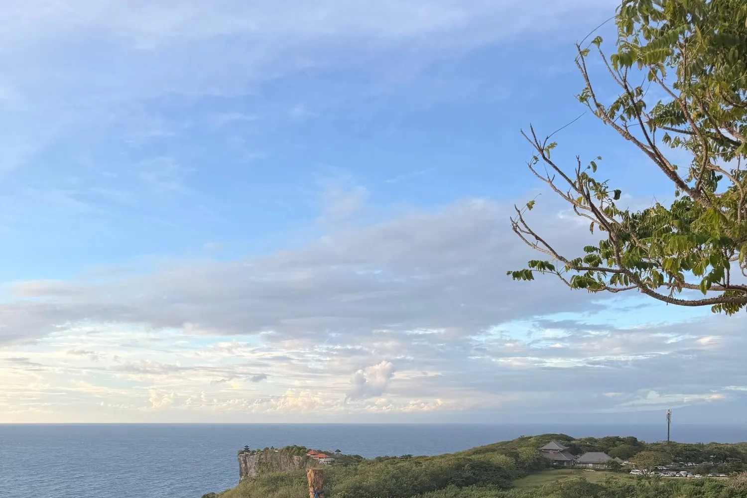 The clifftop coastline of Uluwatu, Bali, with the ocean below and a temple on the green headland.