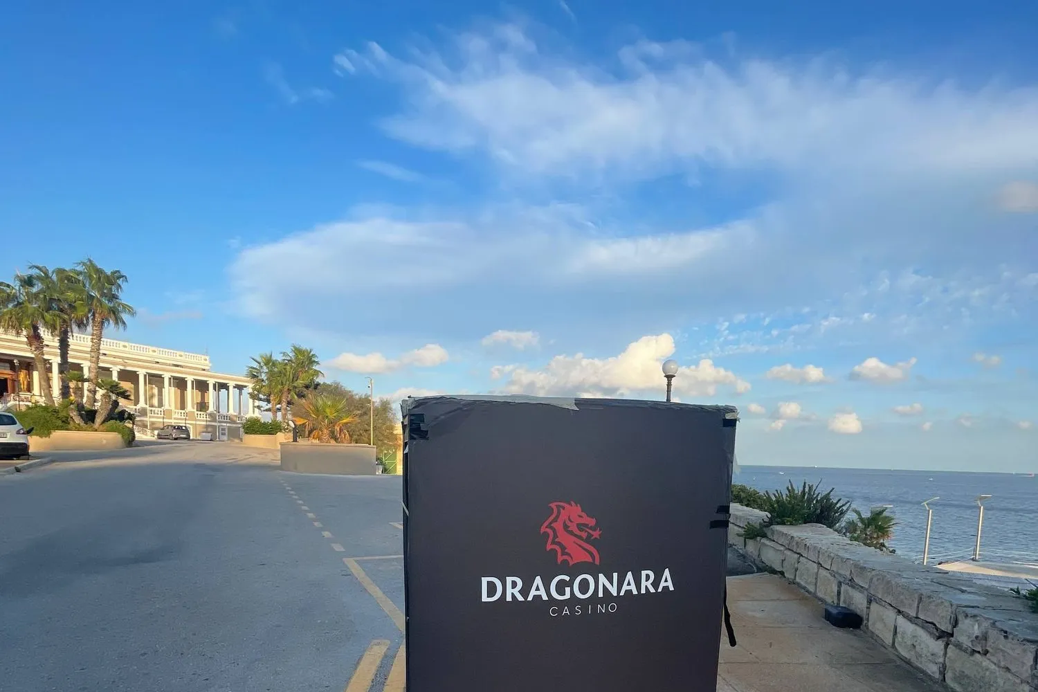 The Dragonara Casino sign on the St Julian's seafront promenade in Malta, blue sky and sea behind.