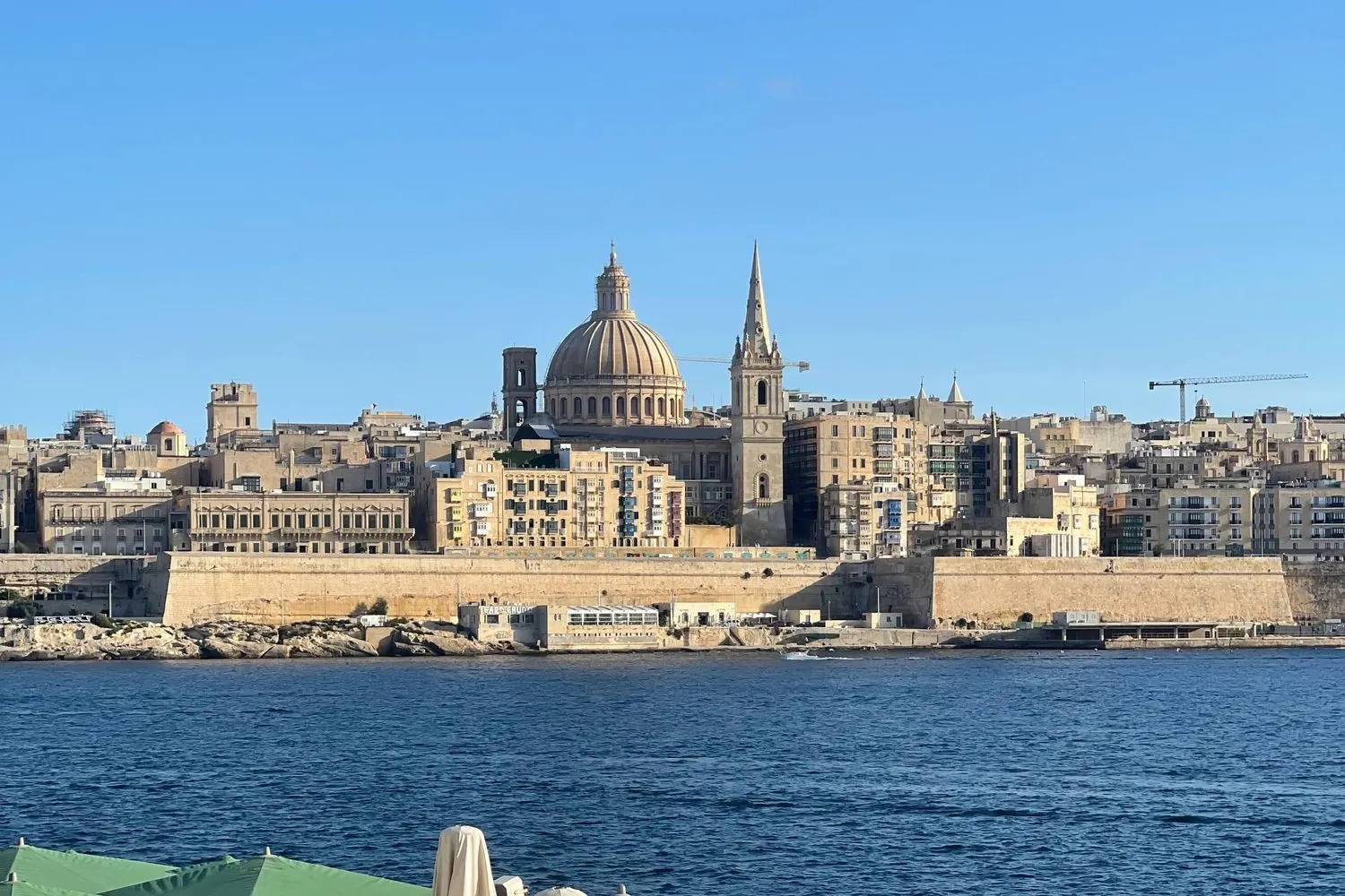 The Valletta skyline with its dome and spire seen across the harbour from a Sliema lido in Malta.