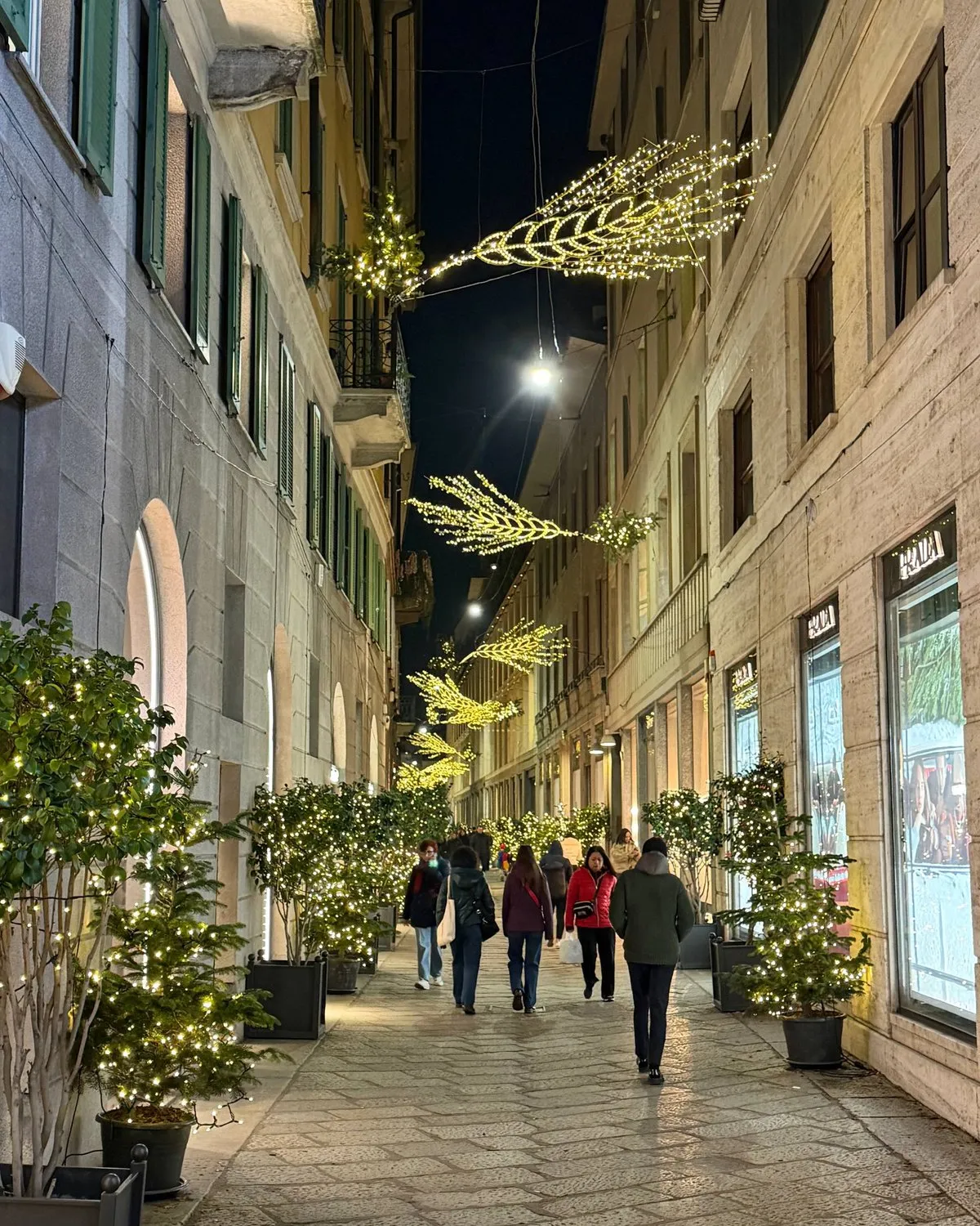 A Milan shopping street at night lit with golden Christmas light installations.