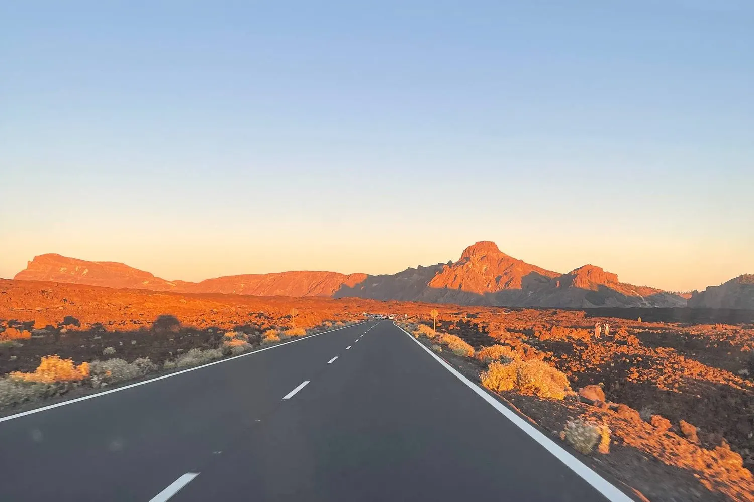 An empty road running toward the red volcanic peaks of Teide at sunset, Tenerife.