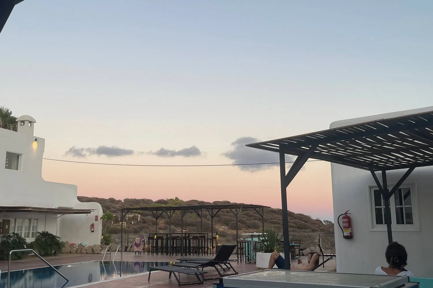 A whitewashed villa hostel with a pool, bar stools, and a pergola at dusk in southern Tenerife.